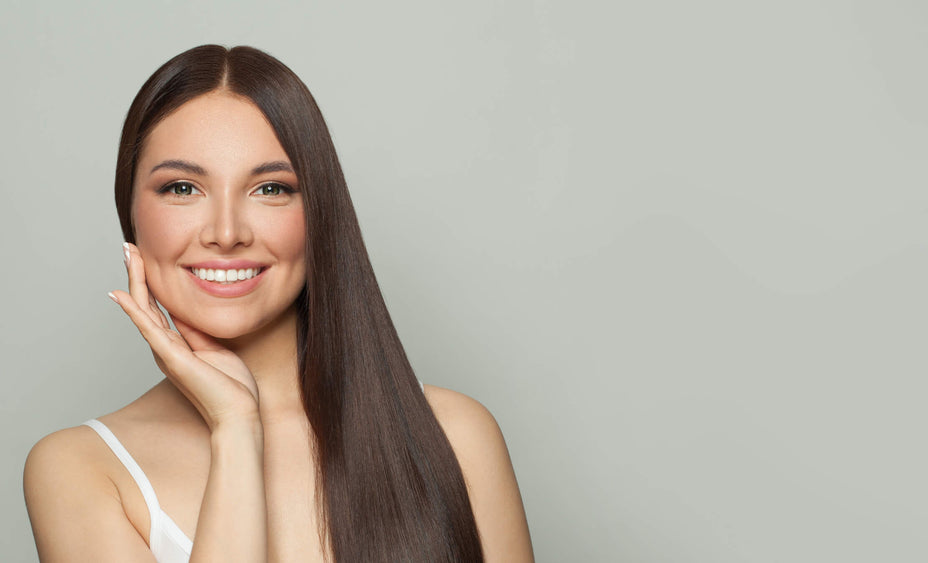 Frau mit langen braunen Haaren, lächelnd – Gesundes, glänzendes Haar, präsentiert durch effektives Haarstyling und hochwertige Pflegeprodukte.